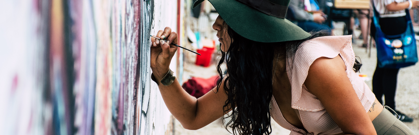 Person with long hair wearing a hat painting a mural outside