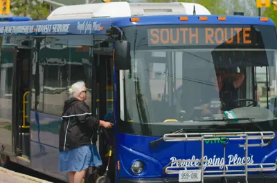 A Midland Penetanguishene Transit Service bus stopped at a curb, displaying “South Route” on the front sign, as a passenger boards through the front door.