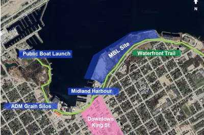A satellite map of Midland’s waterfront highlighting the proposed MBL site in blue, a green route along the shoreline labeled “Waterfront Trail,” and key locations including Midland Harbour, the public boat launch, and ADM grain silos. A pink section marks the downtown King Street area, with roads and neighbourhoods visible throughout.
