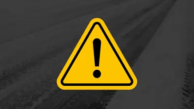 A yellow warning triangle with a black exclamation mark is centered over a background showing snowy, tire‑marked pavement.