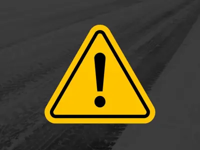 A yellow warning triangle with a black exclamation mark is centered over a background showing snowy, tire‑marked pavement.